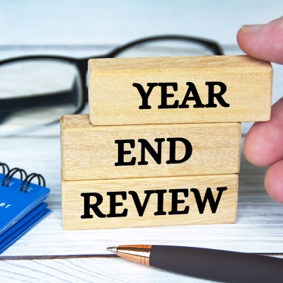 Three building blocks with the words “Year End Review” written on them are lying on some papers next to a pen and a pair of glasses.